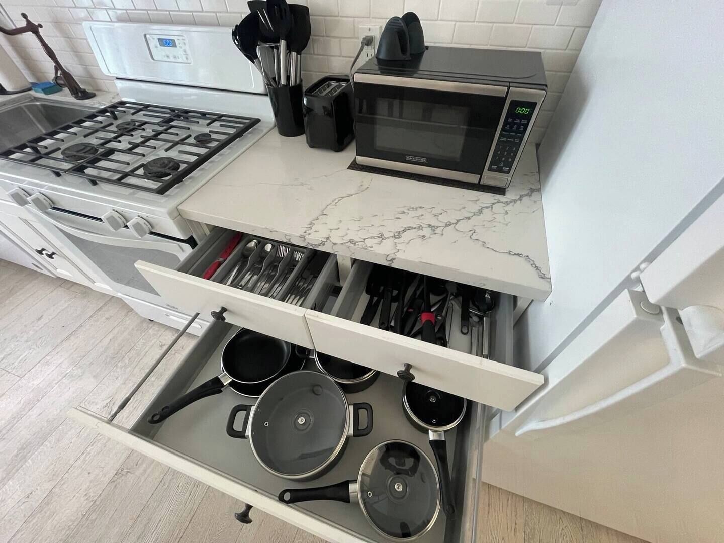 Una cocina con estufa a gas, microondas y un cajón con ollas y sartenes.