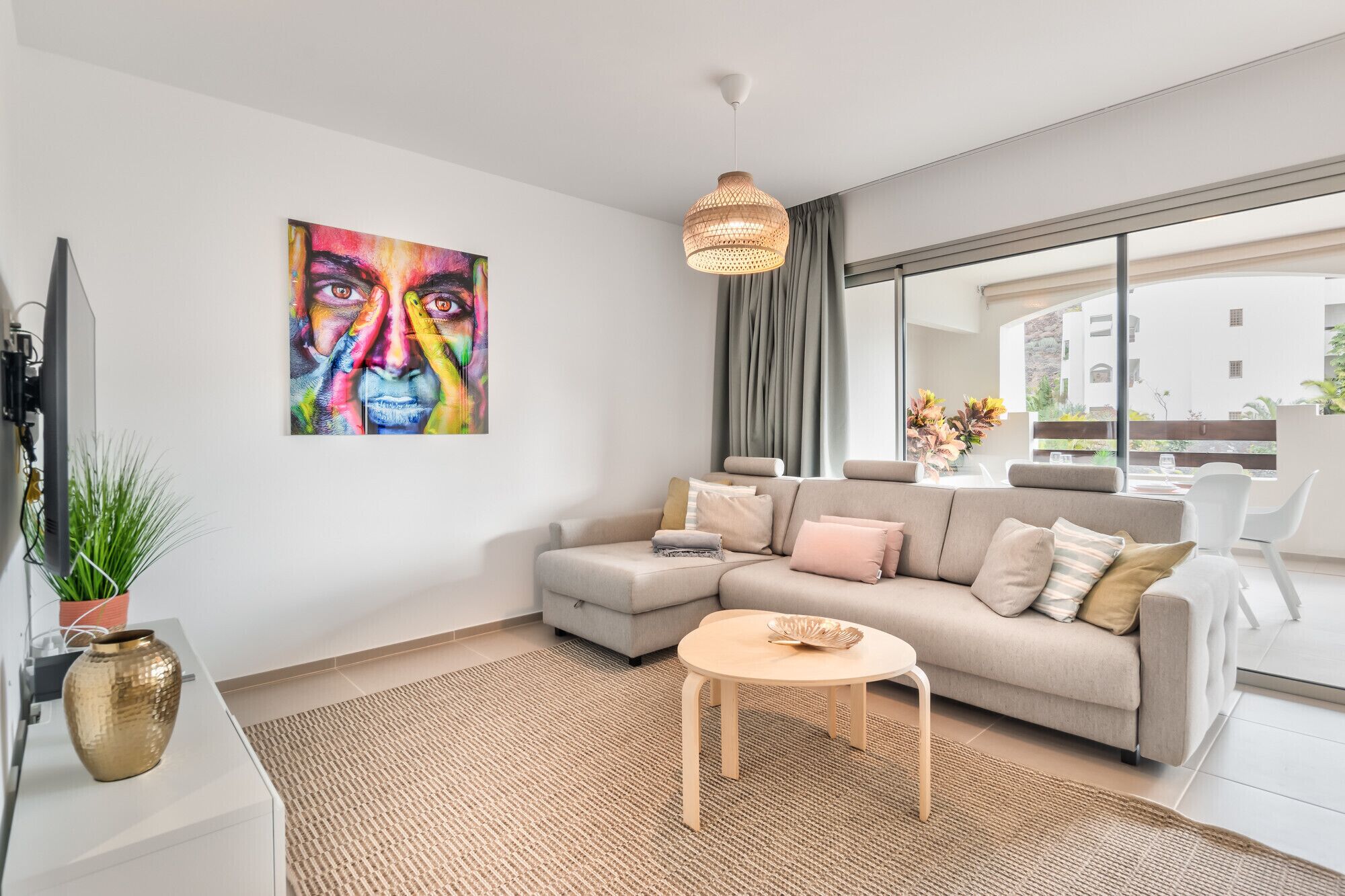 A modern living room with a sofa, a small round table, a hanging light fixture, a large window, and a painting on the wall.