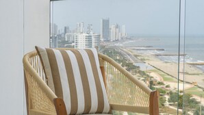 A wicker chair with a striped pillow, positioned in front of a large window overlooking a cityscape and beach. - Seaside Serenity and Style (Cartagena de Indias)