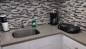 Eine Küche mit weißen Schränken, einer Edelstahl-Spüle, einer Kaffeemaschine und einem schwarzen Wasserkocher.