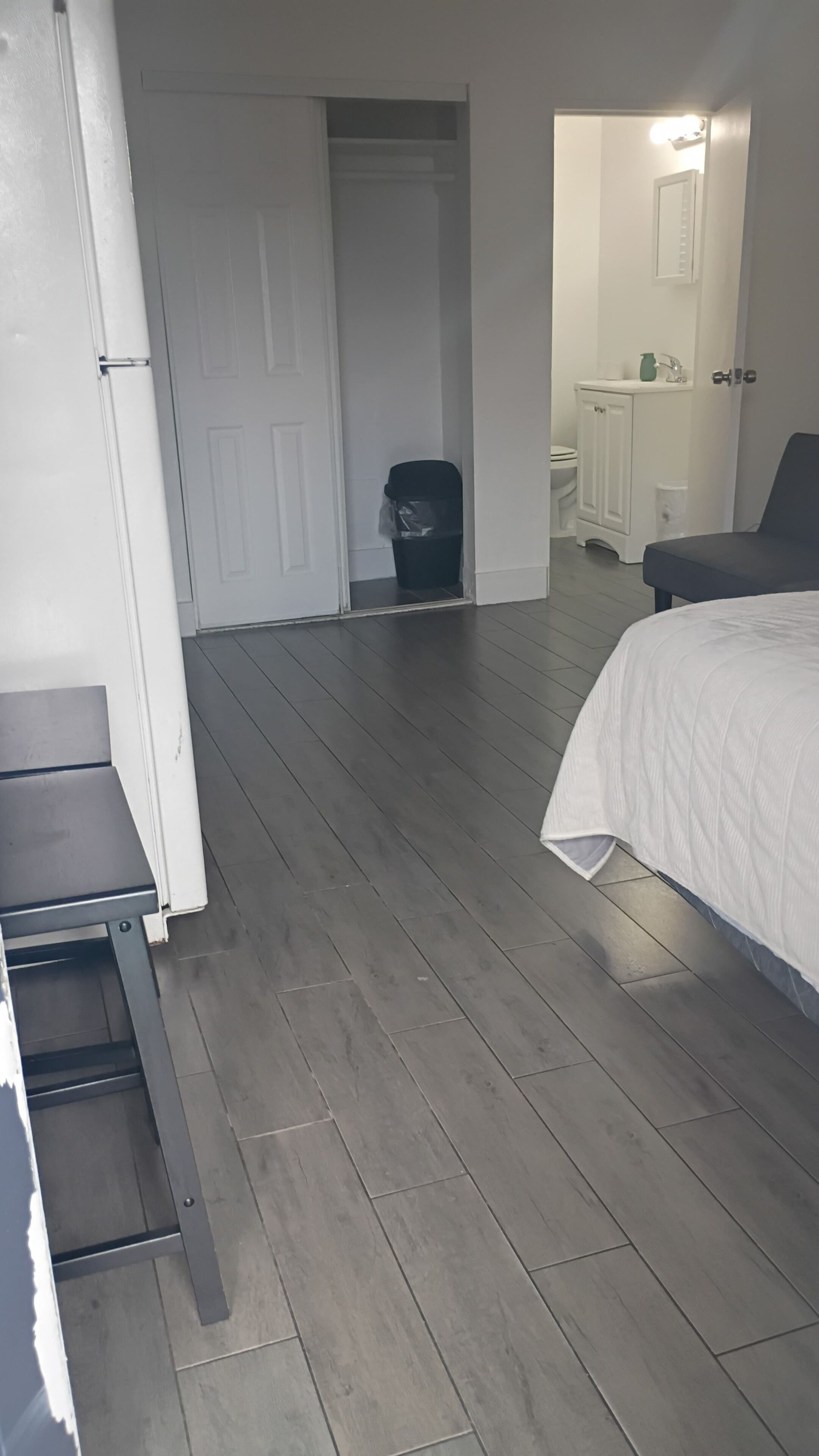Ett sovrum med en säng, ett skrivbord, en stol, en dörr som leder till ett badrum och en papperskorg.