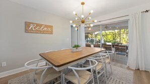 A dining area with a wooden table, white chairs, a ceiling light fixture, and a sign on the wall.