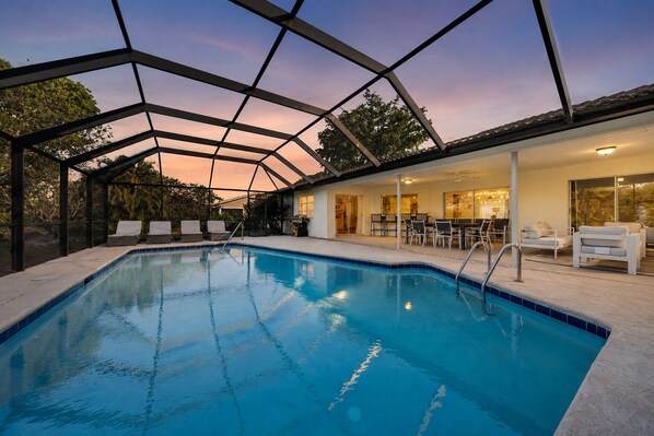 A swimming pool with a covered area, lounge chairs, and a dining area with tables and chairs.