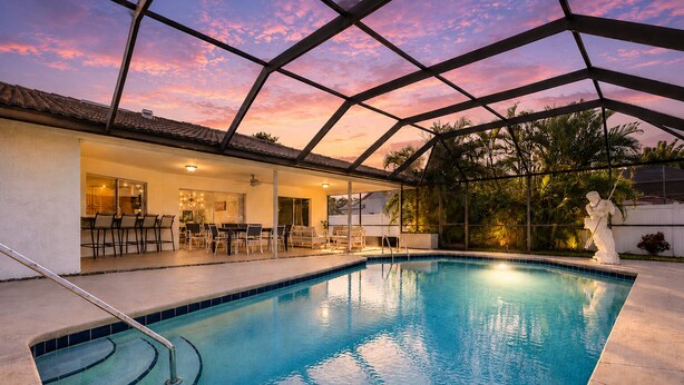 An indoor swimming pool with a covered patio area, a statue, and a sunset view.