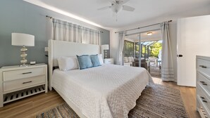 A bedroom with a bed, nightstands, a ceiling fan, and a view of an outdoor patio.