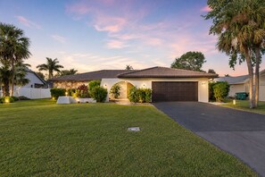 A residential house with a garage, well-maintained lawn, and palm trees.