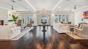 Un salon spacieux doté d’un parquet en bois foncé, de canapés blancs, d’une table basse centrale et d’un lustre.