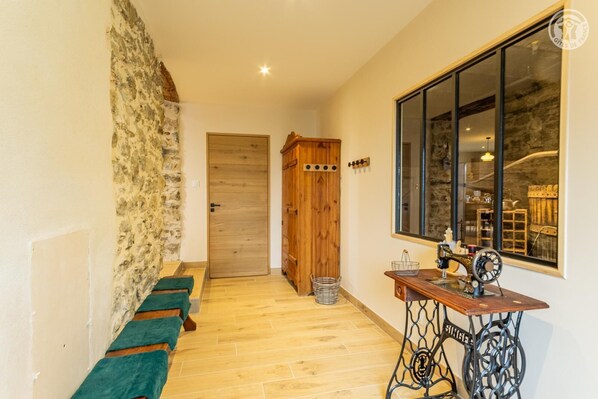 A narrow hallway with a wooden door, a green bench, and a sewing machine on a table.
