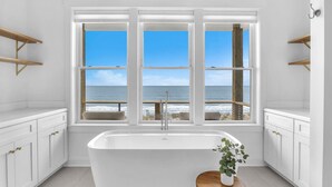 A modern bathroom with a freestanding bathtub, white cabinetry, and a view of the ocean through large windows. - Oceanfront Luxury | 4BR w/ Elevator sleeps 12 (North Topsail Beach)
