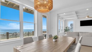 A spacious room with a large wooden table, white walls, and large windows offering a view of the ocean. - Oceanfront Luxury | 4BR w/ Elevator sleeps 12 (North Topsail Beach)
