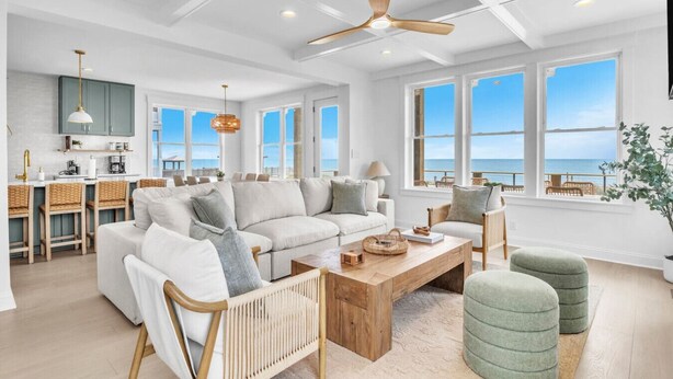 A spacious living room with a large sofa, a coffee table, and a view of the ocean through large windows. - Oceanfront Luxury | 4BR w/ Elevator sleeps 12 (North Topsail Beach)