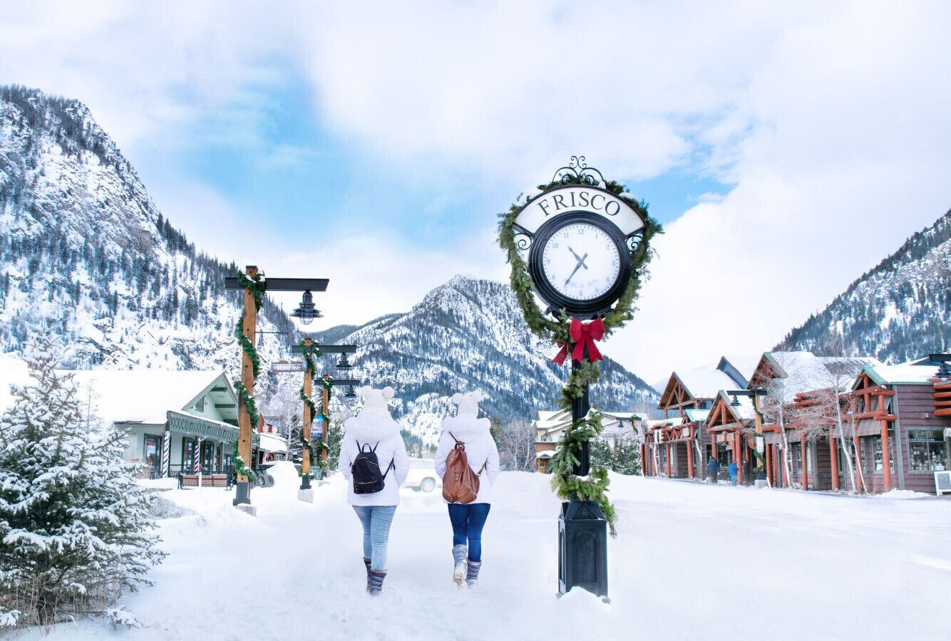 A snow-covered town square with a clock labeled "FRISCO" and traditional wooden buildings.