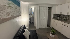 Uma cozinha moderna com armários brancos e painel de azulejos, um sofá preto com uma almofada branca, e um quadro com uma cena de praia na parede.