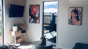 A modern living room with a wooden ceiling, a flat-screen TV, a round coffee table, a sofa, and a large window with a view of mountains.