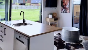 A modern kitchen with a large island, a dishwasher, and a window overlooking a grassy area.