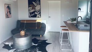 A modern living room with a sofa, a coffee table, and a kitchen area with a sink and bar stool.