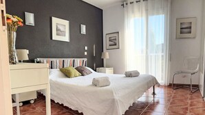 A bedroom with a bed, a nightstand, a chair, and a window with curtains.
