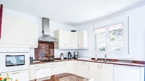 A modern kitchen with white cabinets, a granite countertop, a built-in oven, a coffee maker, and a window with a view of greenery.