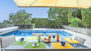 A poolside dining area with a table set for breakfast, overlooking a swimming pool.