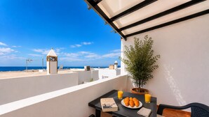 Un balcon avec une table préparée pour le petit-déjeuner, une plante en pot et une vue sur la mer.