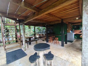 A covered outdoor area with wooden tables and stools, a bench, and a refrigerator. - Vista Rio Celeste Cabin (Provincia de Alajuela)