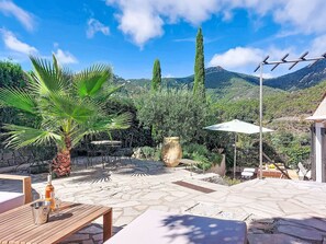 A patio with stone flooring, outdoor furniture, a palm tree, and a view of a mountainous landscape. - Sainte Honorine by Interhome (Théoule sur mer)