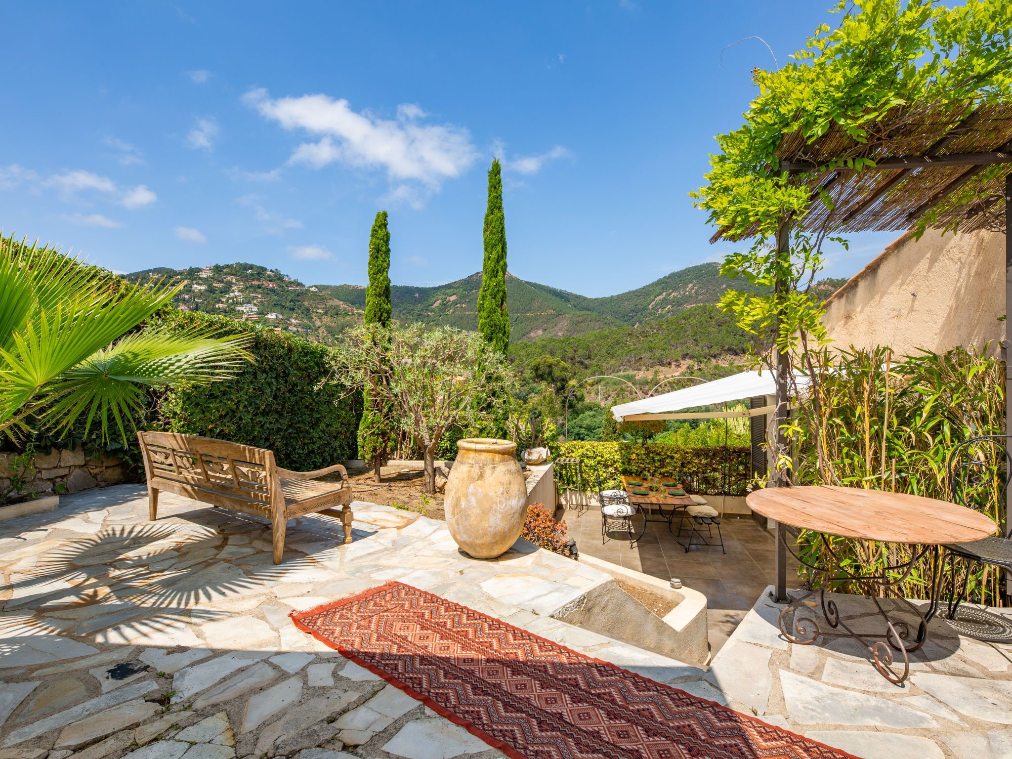 A stone patio with a wooden bench, a large pot, and a table with chairs.