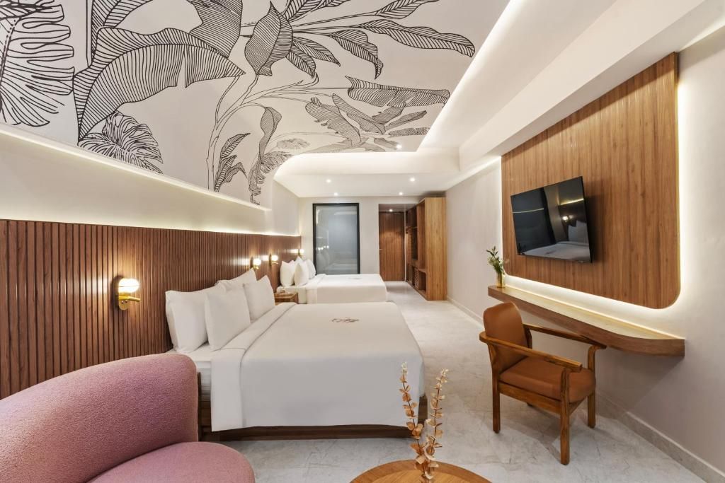 A modern hotel room with a large bed, a desk, a chair, and a TV mounted on the wall.
