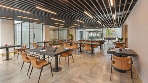 A modern dining area with tables and chairs, large windows, and a ceiling with linear lighting fixtures. - Zana By The Ganges, Rishikesh (Narendranagar)