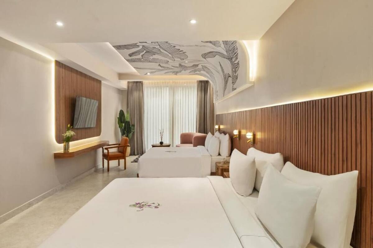 Una habitación de hotel moderna con una cama grande, una zona de estar, un televisor montado en la pared y un techo decorativo.