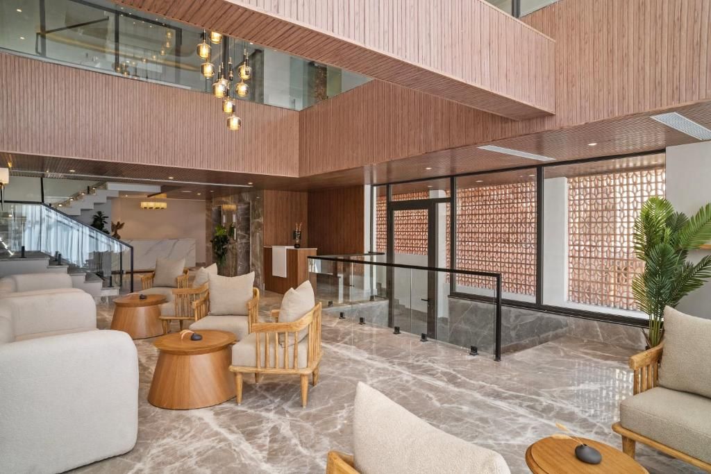 A spacious lobby with a high ceiling, wooden paneling, and a marble floor. There are multiple seating areas with sofas and chairs, and a staircase leading to an upper level.