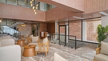 A spacious lobby with a high ceiling, wooden paneling, and a marble floor. There are multiple seating areas with sofas and chairs, and a staircase leading to an upper level.
