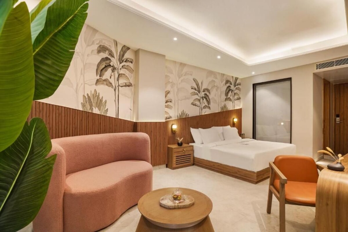 A modern hotel room with a large bed, a pink sofa, a wooden nightstand, and a round coffee table.