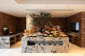 A buffet area with a marble island, various food items, and a decorative tree. - Zana By The Ganges, Rishikesh (Narendranagar)