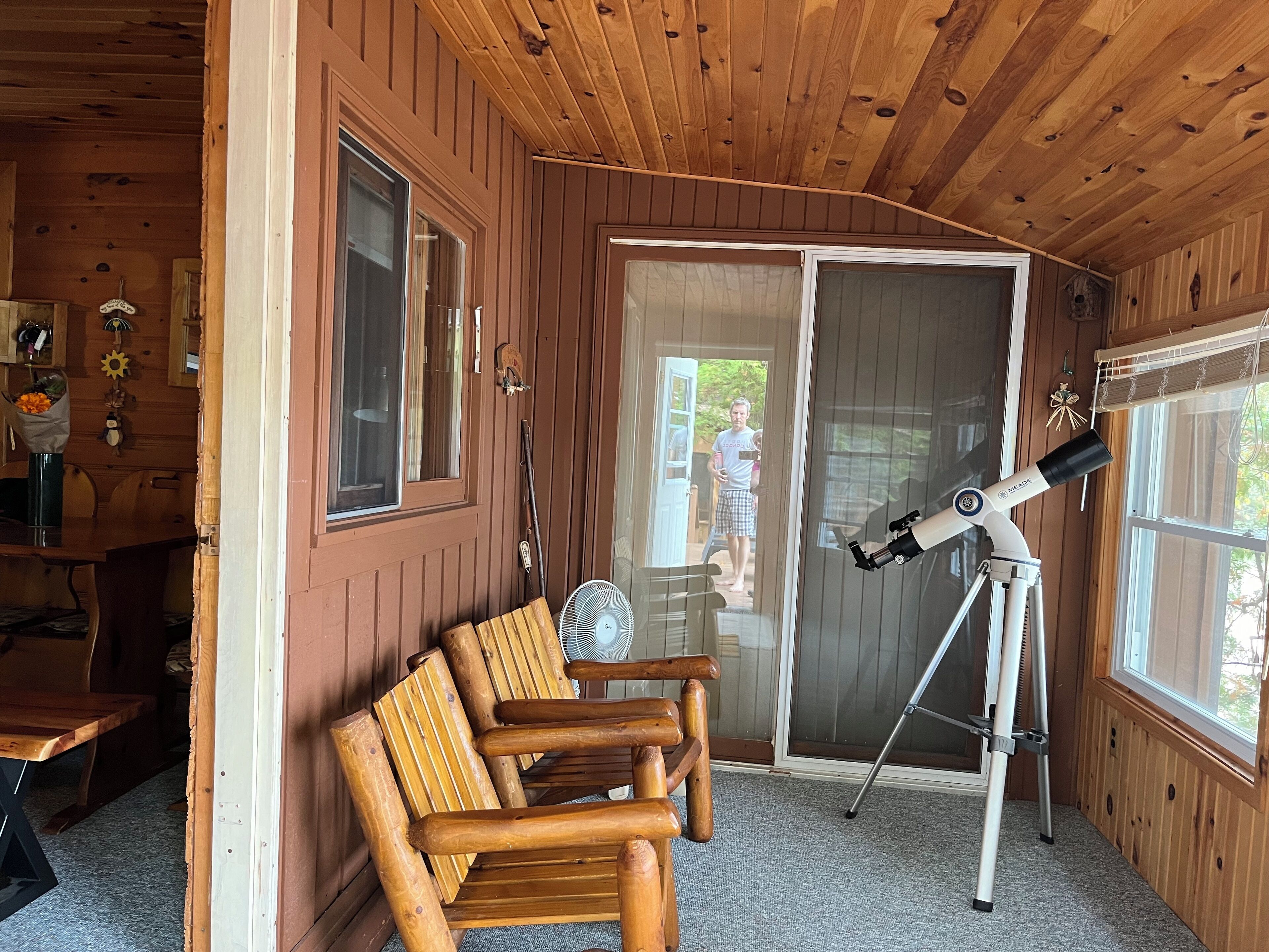 Interior de una cabaña de madera con un telescopio, sillas de madera y una zona de comedor.