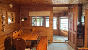 A wooden cabin interior with a dining table, chairs, a telescope, and a large window. - Peaceful Waterfront Cottage on Ottawa River – Nature Lover’s Retreat! (Westmeath)