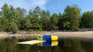 A clear view of a lake with a floating platform and a yellow and blue buoy. - Peaceful Waterfront Cottage on Ottawa River – Nature Lover’s Retreat! (Westmeath)