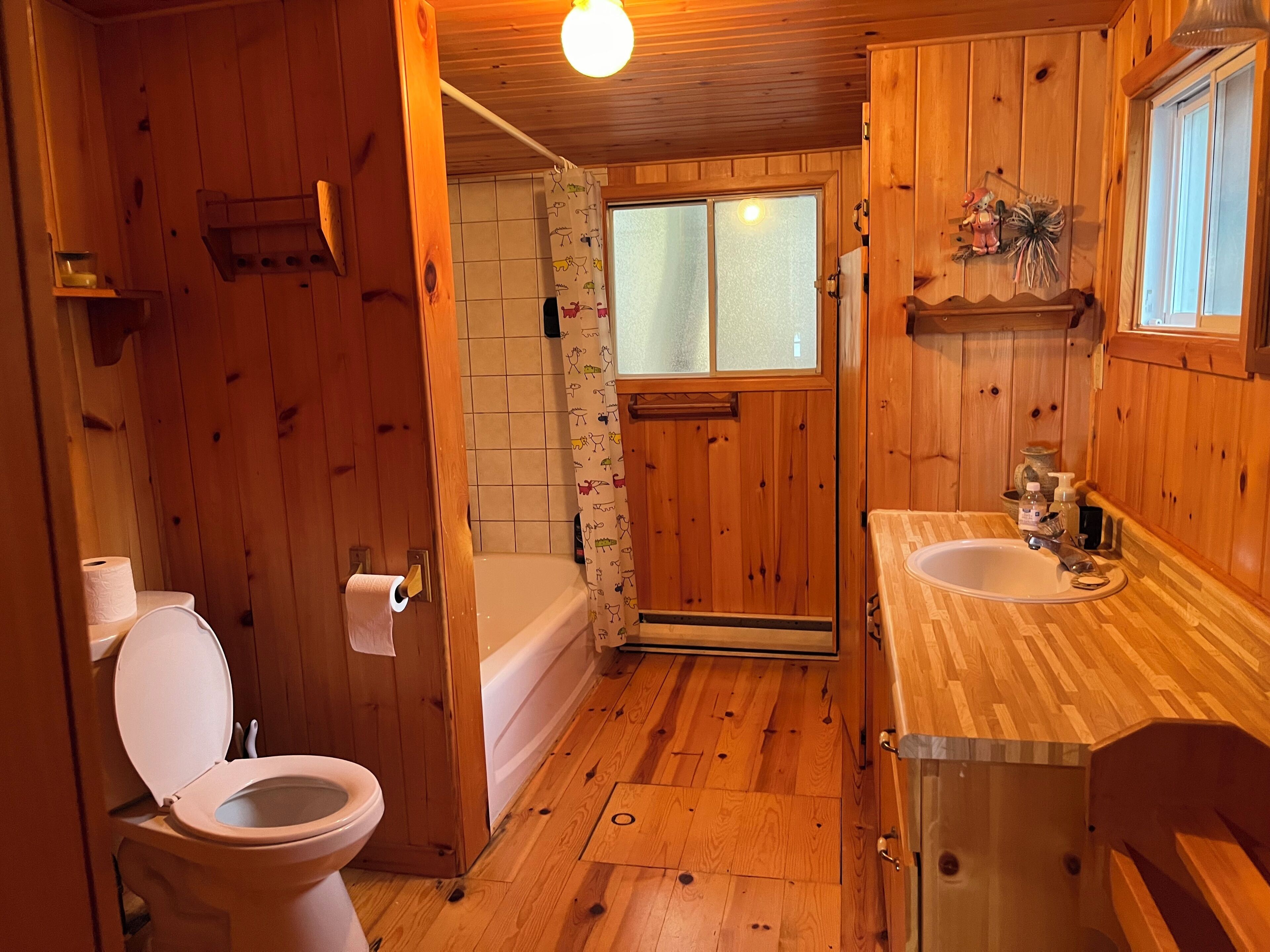 A wooden cabin bathroom with a toilet, sink, and shower.