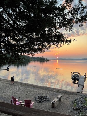 A lakeside scene with a sunset, boats, and a dock.