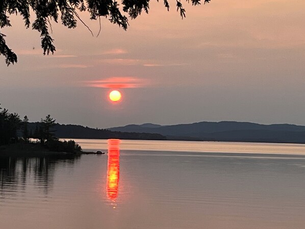 A sunset over a calm lake with distant mountains.