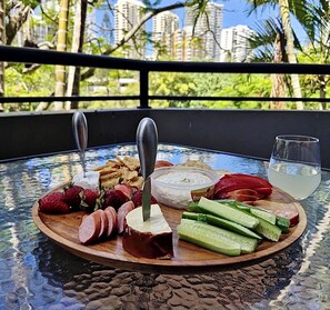 A table with a cheese board, fruits, and a drink, set on a balcony with a city view. - Serenity in Surfers Paradise (Surfers Paradise)