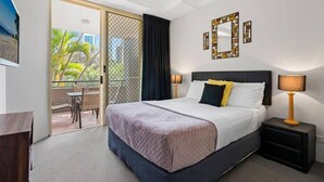A hotel room with a bed, bedside lamps, a mirror, and a view of a balcony with outdoor seating.