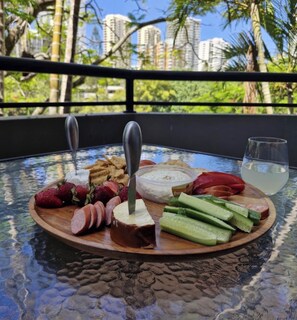 A wooden board with various foods and a glass of water on a glass table with a view of buildings and trees. - Serenity in Surfers Paradise (Surfers Paradise)