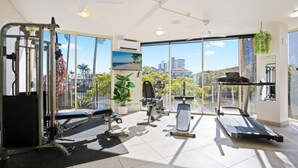 A gym with various exercise equipment, large windows, and a view of buildings and trees.