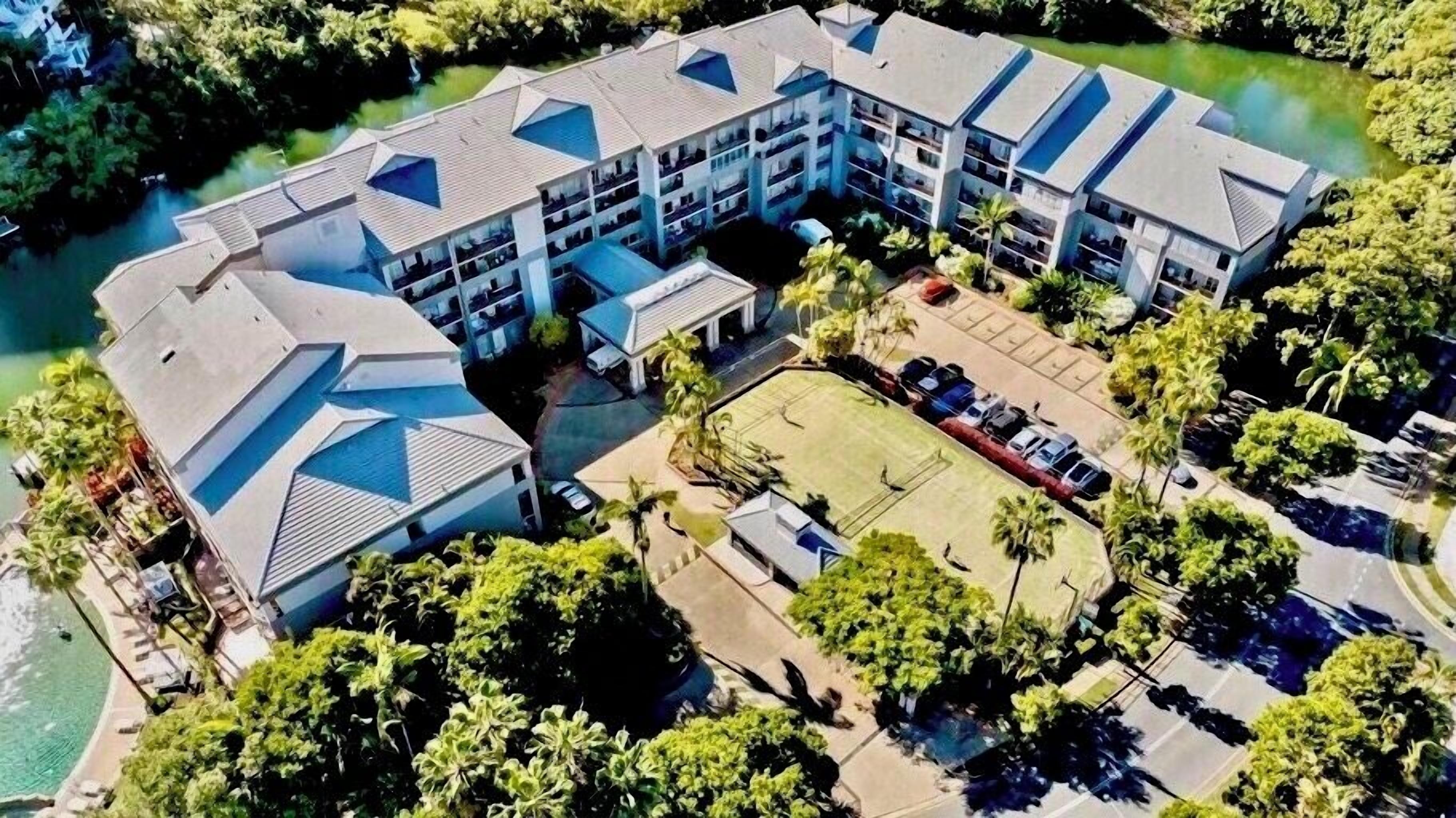 A multi-story hotel with a central courtyard, surrounded by lush greenery and a body of water.