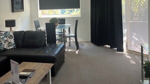 A modern living room with a black sofa, a wooden coffee table, and a dining area with a glass table and chairs.