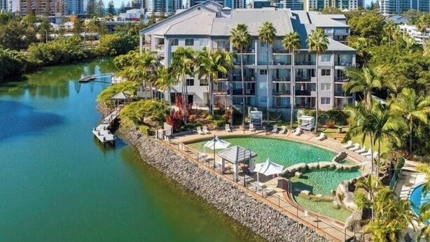 A hotel with a pool, surrounded by palm trees and a city skyline in the background.