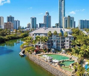 A hotel with a pool, surrounded by palm trees and a city skyline in the background. - Serenity in Surfers Paradise (Surfers Paradise)