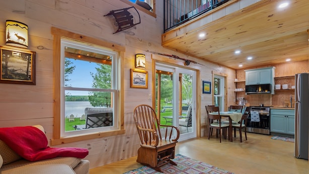 A cozy cabin interior with a dining area, kitchen, and a large window overlooking a garden.