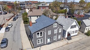 A multi-story residential building with a grey roof, a front porch, and a driveway with parked cars.
